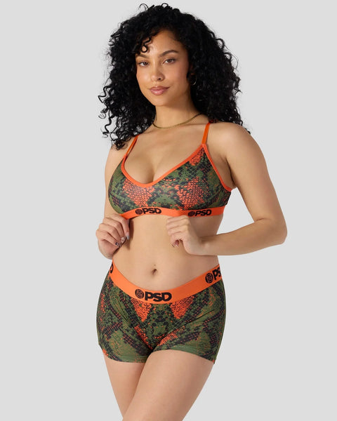 Woman wearing green and red snake-scale patterned sports bra and shorts set with orange trim and branding.