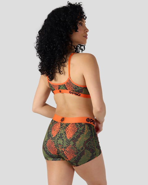Woman wearing orange and green snake-pattern sports bra and matching shorts with PSD branding.