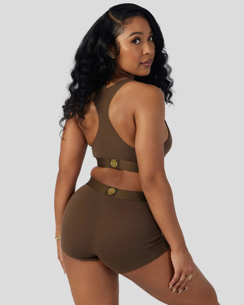 Woman wearing cocoa-colored racerback sports bra and matching high-waisted shorts with gold buckle details.