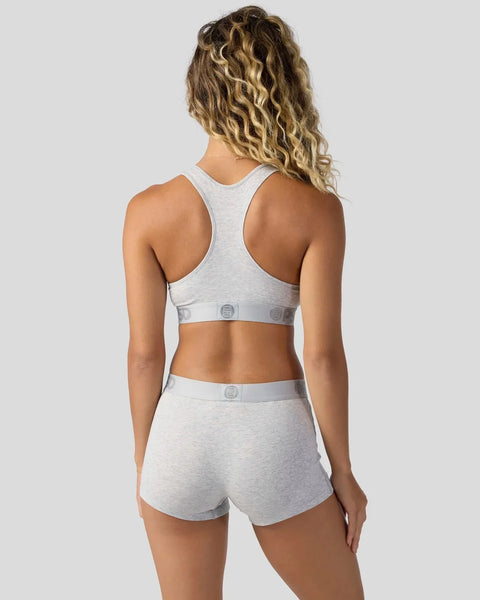 Woman wearing light gray racerback sports bra and matching shorts with branded waistband, shown from back.