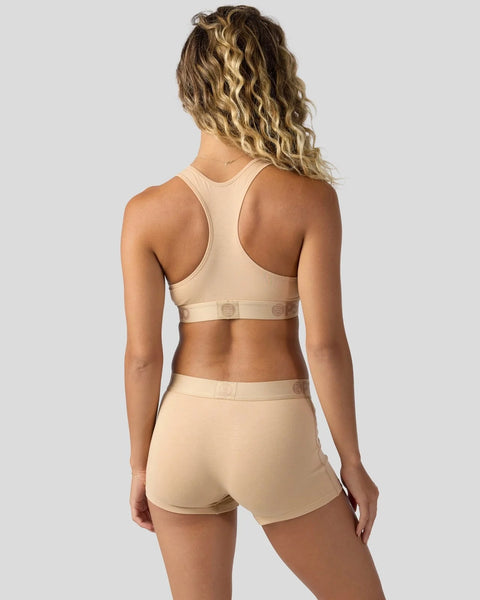 Woman wearing a beige racerback sports bra and matching shorts with visible waistband labels.