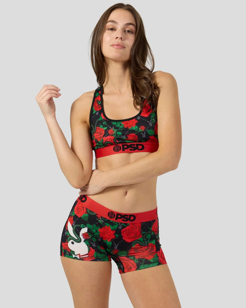 Woman wearing black sports bra and shorts with red roses and green leaves print, red waistband with PSD branding.