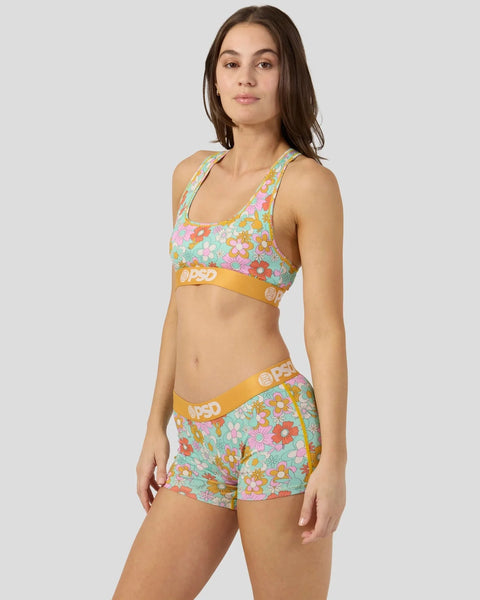 Woman wearing multicolored floral sports bra and matching shorts with yellow waistband trim.