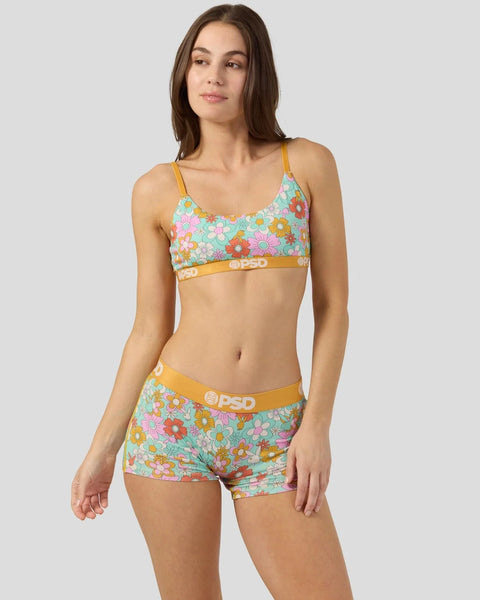 Woman wearing colorful floral bra and boy shorts set with yellow waistbands and logo details.