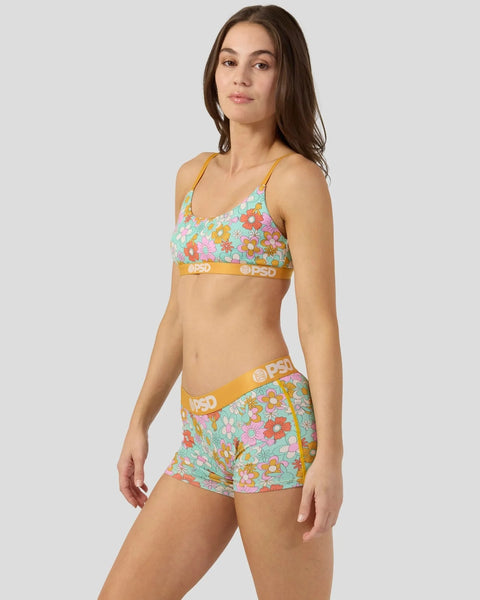 Woman wearing turquoise bralette and shorts with colorful floral print and gold trim.