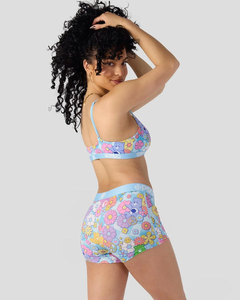 Woman wearing two-piece swimsuit with colorful flower and Care Bears print on light blue background.
