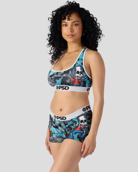 Woman wearing PSD sports bra and shorts with skull and character print in turquoise, black, and orange.