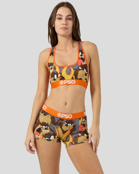 Woman wearing Taz character print sports bra and shorts set with orange trim and PSD branding.