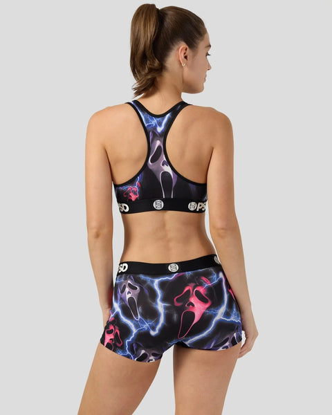 Woman wearing black sports bra and shorts with blue lightning and pink ghost face print design, shown from back view.