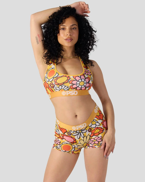 Woman wearing yellow sports bra and shorts with multicolored floral print and branded waistband.