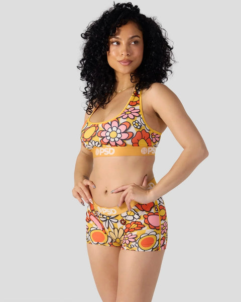 Woman wearing yellow sports bra and shorts with multicolored floral print pattern.