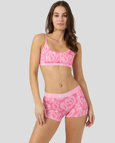 Woman wearing pink patterned sports bra and matching shorts with all-over logo print.