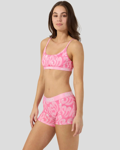 Woman wearing bright pink sports bra and matching shorts with abstract bubble letter print.
