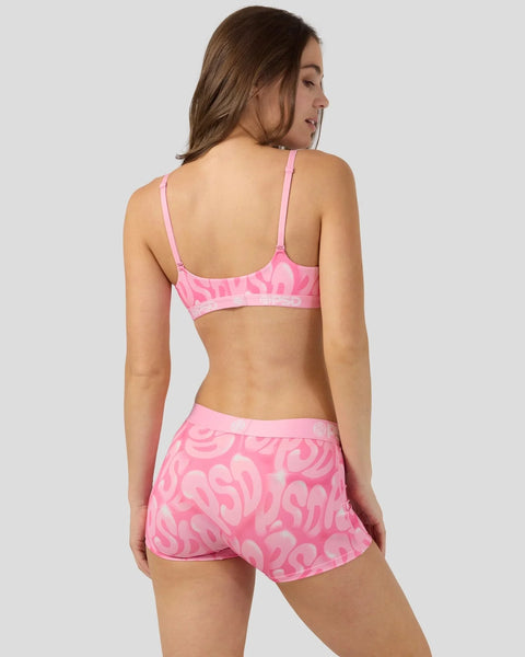Woman wearing pink patterned two-piece swimsuit with spaghetti straps and matching shorts, shown from back view.