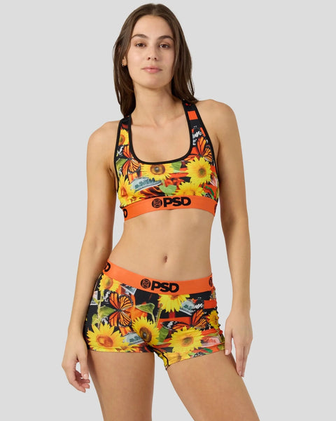 Woman wearing a two-piece set with colorful sunflower and butterfly print, orange waistband with PSD logo, and black racerbac