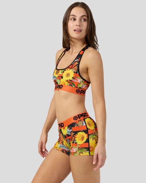 Woman wearing a two-piece set with sunflower and floral pattern in yellow, red, and black with orange elastic waistbands.