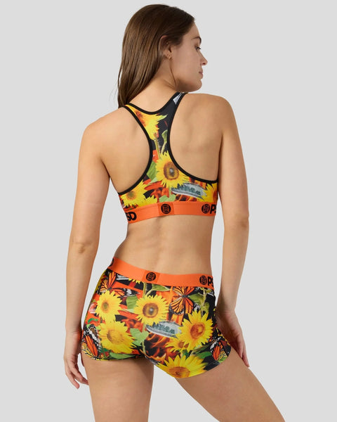 Woman wearing a two-piece athletic set with sunflower and butterfly print, orange elastic bands, and black racerback top, sho