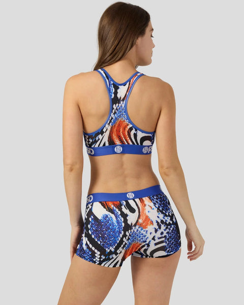 Woman wearing blue sports bra and matching shorts with snake scale and orange pattern print.