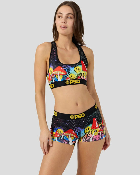 Woman wearing black sports bra and shorts with colorful mushroom and smiley face print, PSD waistband.