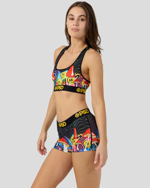 Woman wearing colorful mushroom-print sports bra and matching shorts with black straps and yellow logo bands.