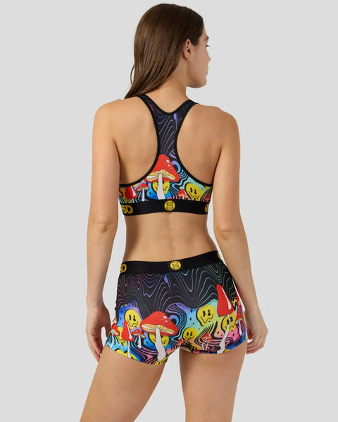 Woman wearing black sports bra and matching shorts with colorful mushroom and smiley face print, shown from back view.