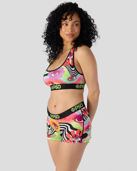 Woman wearing colorful eye-print sports bra and shorts set with neon green, pink, and black design.