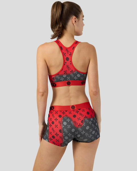 Woman wearing red and gray patterned sports bra and matching shorts with geometric logo design.
