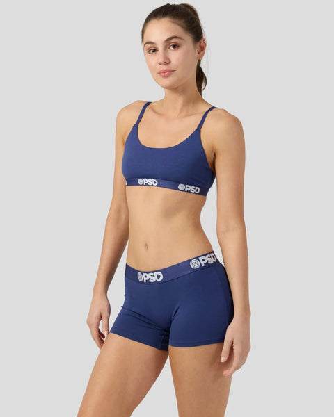 Woman wearing navy sports bra and matching navy shorts with branded waistband.
