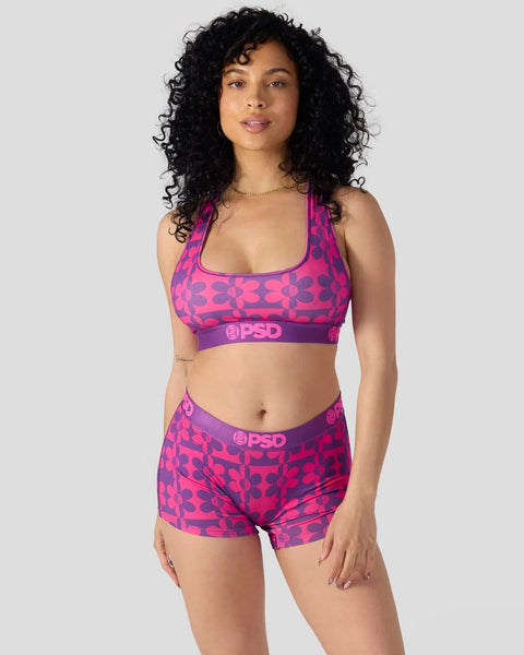 Woman wearing bright pink and purple floral patterned sports bra and matching boy shorts with PSD branding.