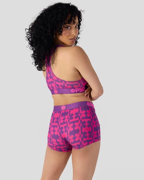 Woman wearing purple and pink patterned racerback sports bra and matching shorts with brand text on waistband.