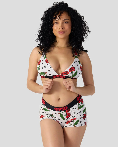Two-piece lingerie set with white fabric featuring red cherry and black heart pattern, black waistband with branding.