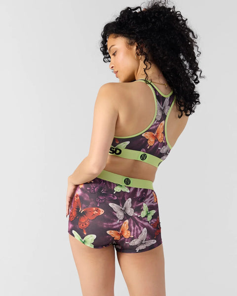 Woman wearing dark purple sports bra and shorts set with colorful butterfly print and neon green trim, shown from back.