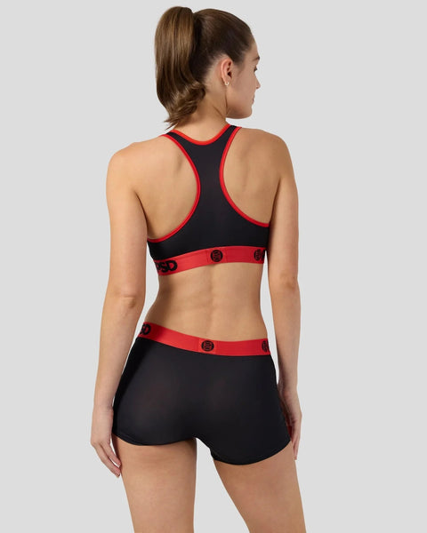 Woman wearing black sports bra and shorts with red trim and button details, shown from back.