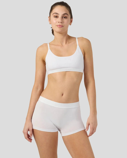 Woman wearing white sports bra and matching white shorts against neutral background.