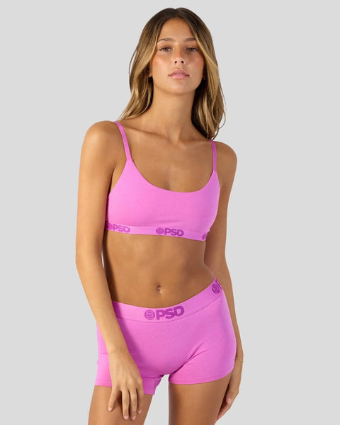 Woman wearing bright pink sports bra and matching shorts with elastic waistband and logo detailing.