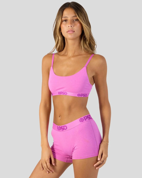 Woman wearing bright pink sports bra and matching shorts with branded waistband.