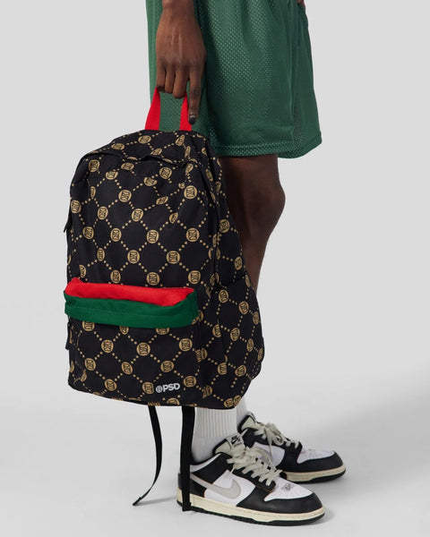 Black backpack with gold emblem pattern, red and green stripe accent, and red handles.