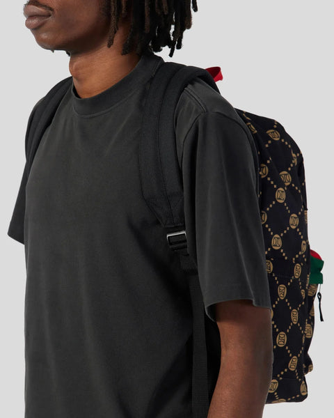Black backpack with monogram pattern and red accent strap worn on person's shoulder.