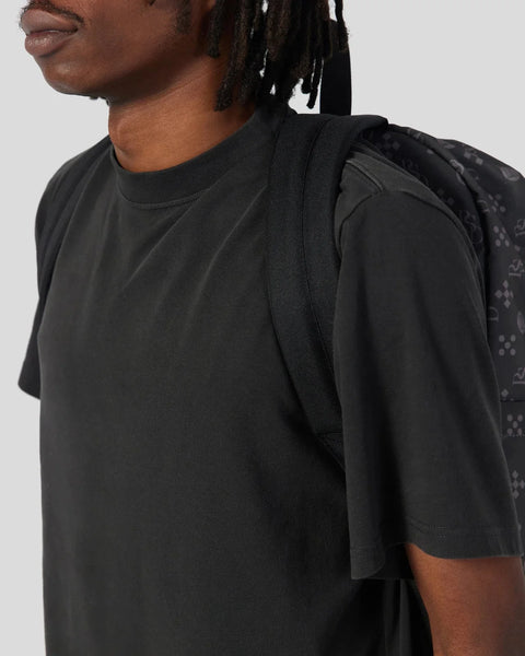 Black backpack with padded straps worn on person's shoulder against neutral background.
