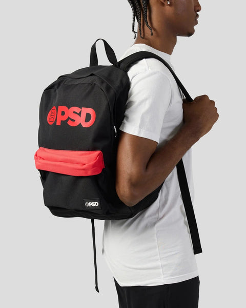 Black backpack with red PSD logo and red front pocket, worn on person's shoulder.