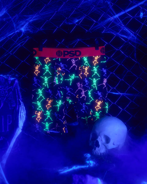 PSD boxers with neon skeleton figures in green, purple, orange and blue on black fabric, displayed on mannequin.