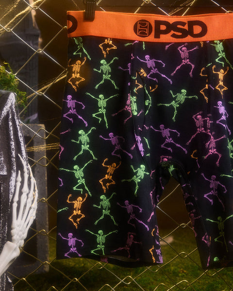 Black briefs with neon skeleton figures in green, purple, orange, and pink throughout, orange PSD waistband.