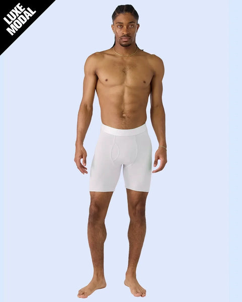 Man wearing white knee-length boxer briefs with elastic waistband and front pouch detail.