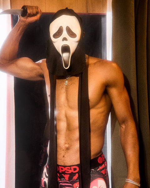 Shirtless man wearing Ghost Face mask and black robe, holding knife above head.