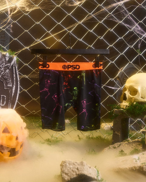 Black boxer briefs with neon skeleton print and orange PSD waistband displayed on mannequin.