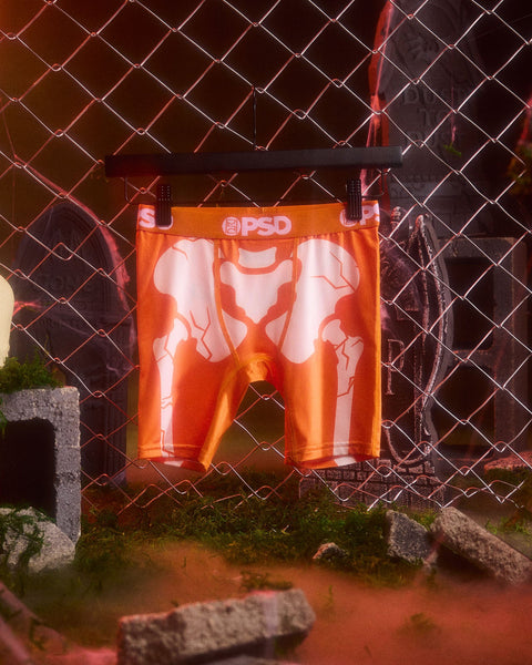 Orange PSD branded boxer shorts with red vein pattern displayed on chain-link fence.
