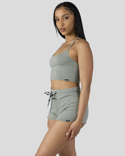 Woman wearing sage green camisole crop top and matching drawstring shorts sleep set.