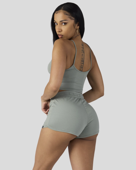 Woman wearing sage green cami sleep set with thin straps and matching shorts, shown from back.