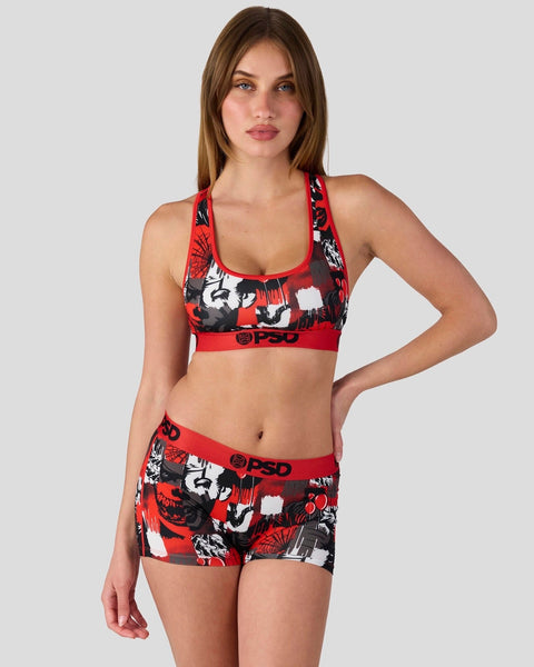 Woman wearing red, black, and white patterned sports bra and matching shorts with graphic print and brand waistband.