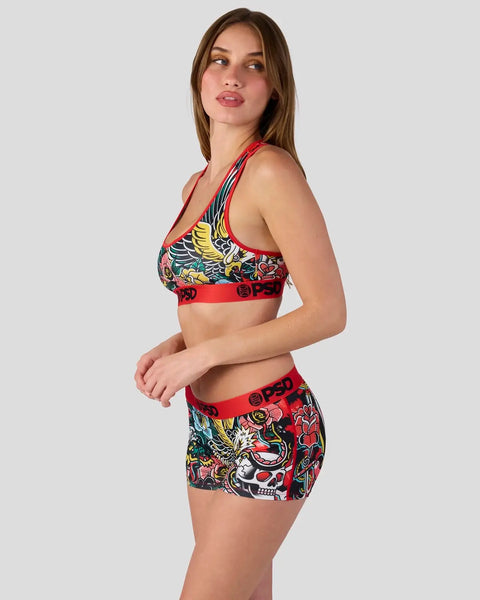 Woman wearing red and multicolor winged graphic sports bra and shorts set with skull and bird designs.